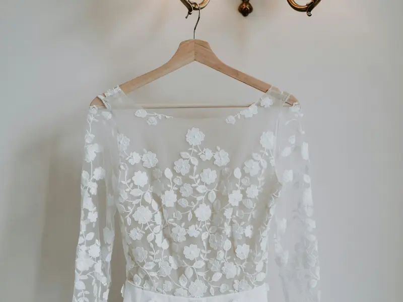 Abito da sposa con maniche lunghe in pizzo appeso a una gruccia di legno