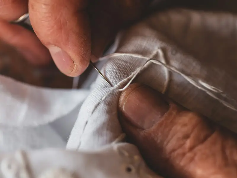Mani che cuciono a mano un tessuto bianco con ago e filo